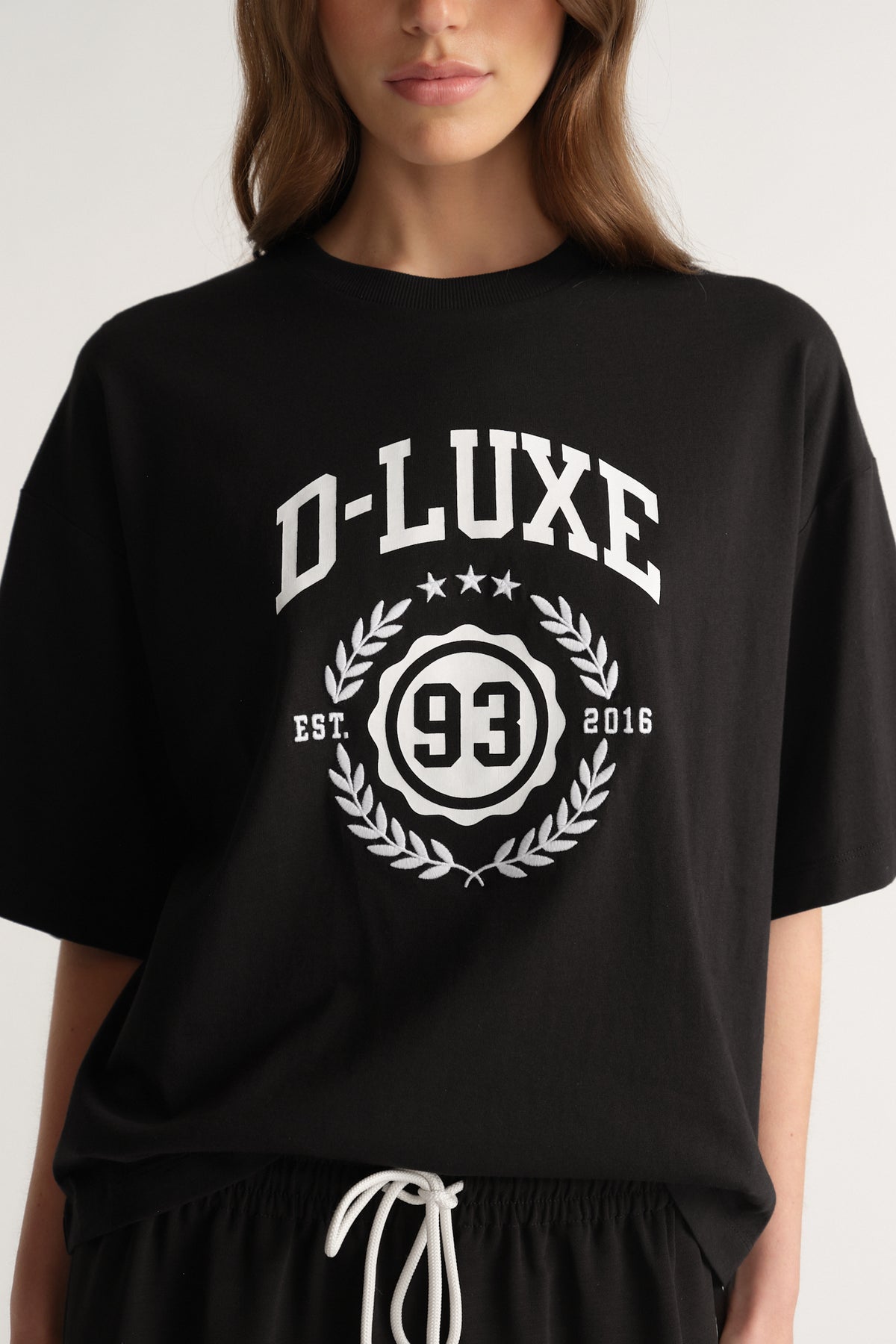 Woman wearing an oversized black D-Luxe graphic tee with a crest print and black drawstring pants