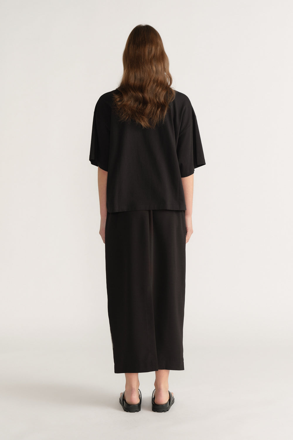 Back view of a woman in an oversized black tee with cropped wide leg pants and black flats