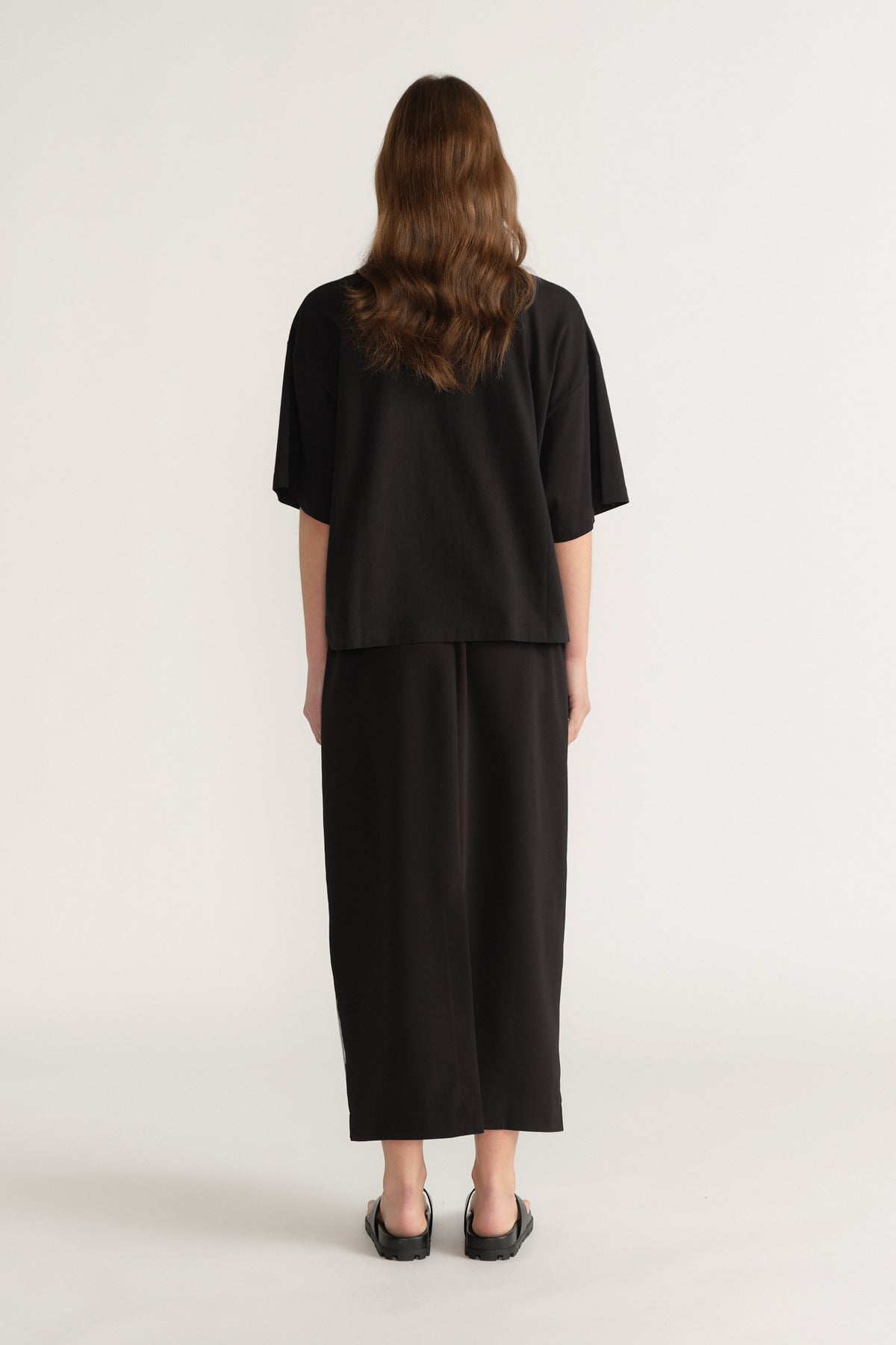 Back view of a woman in an oversized black tee with cropped wide leg pants and black flats