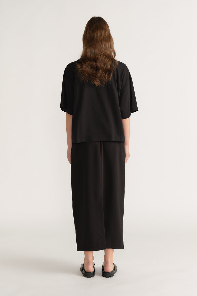 Back view of a woman in an oversized black tee with cropped wide leg pants and black flats