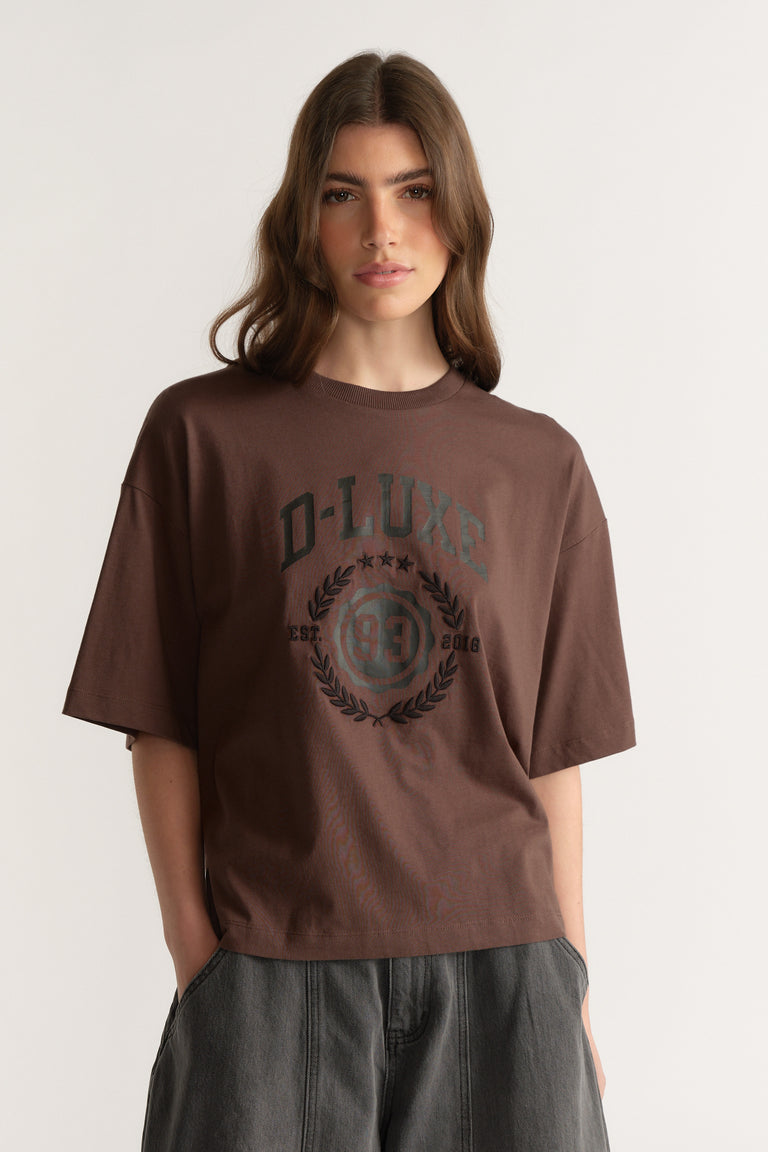 Woman wearing an oversized brown D-Luxe graphic tee with dark jeans