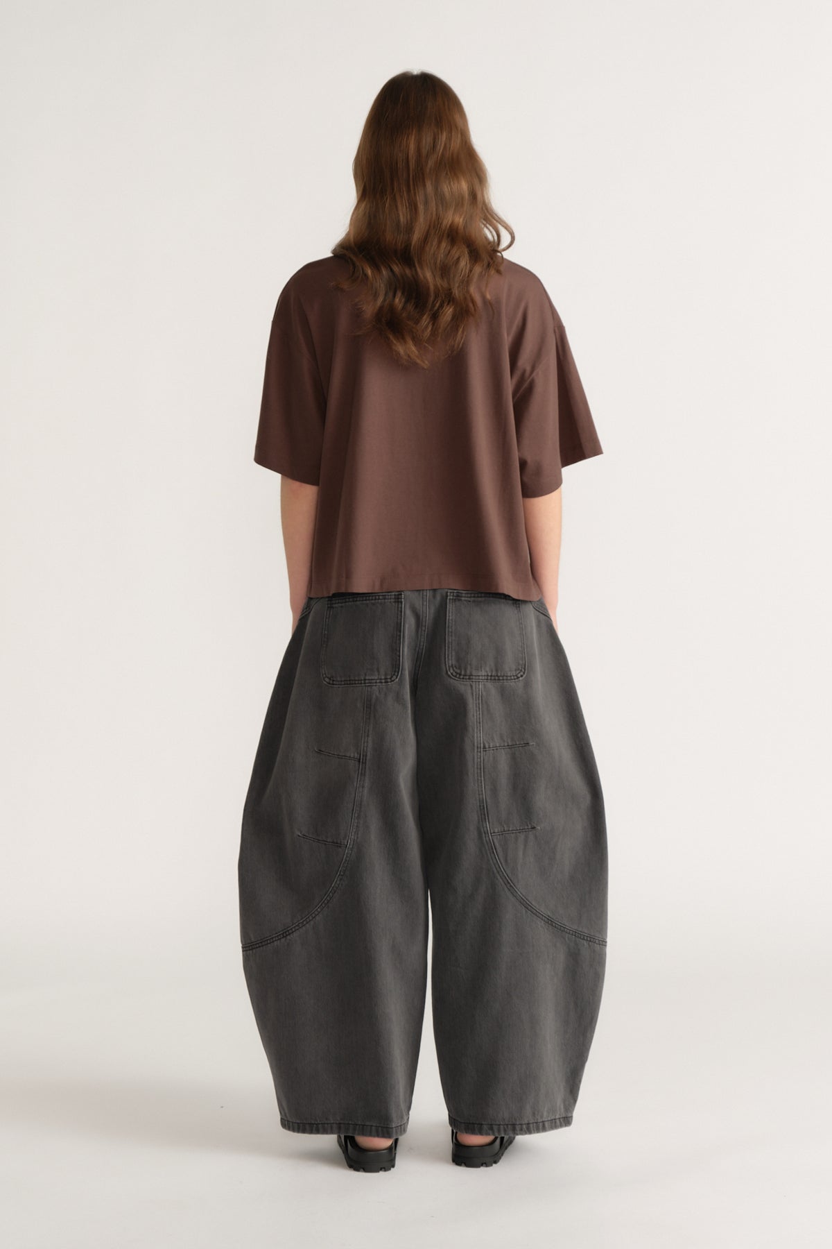 Back view of a model wearing an oversized brown crest print tee with dark barrel leg jeans