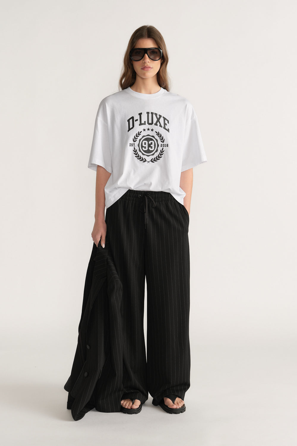 Woman wearing an oversized white D-Luxe graphic tee with black wide-leg pants and sandals