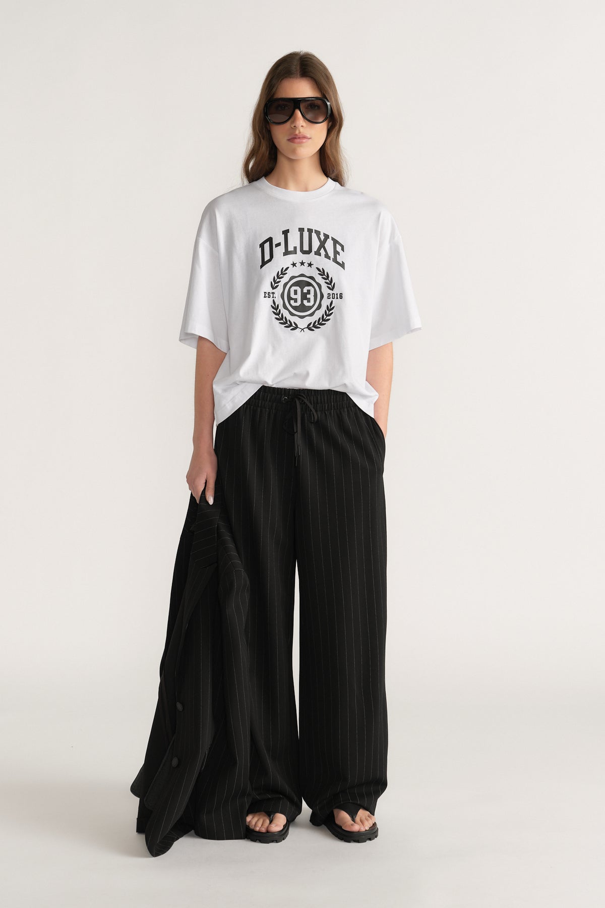 Woman wearing an oversized white D-Luxe graphic tee with black wide-leg pants and sandals