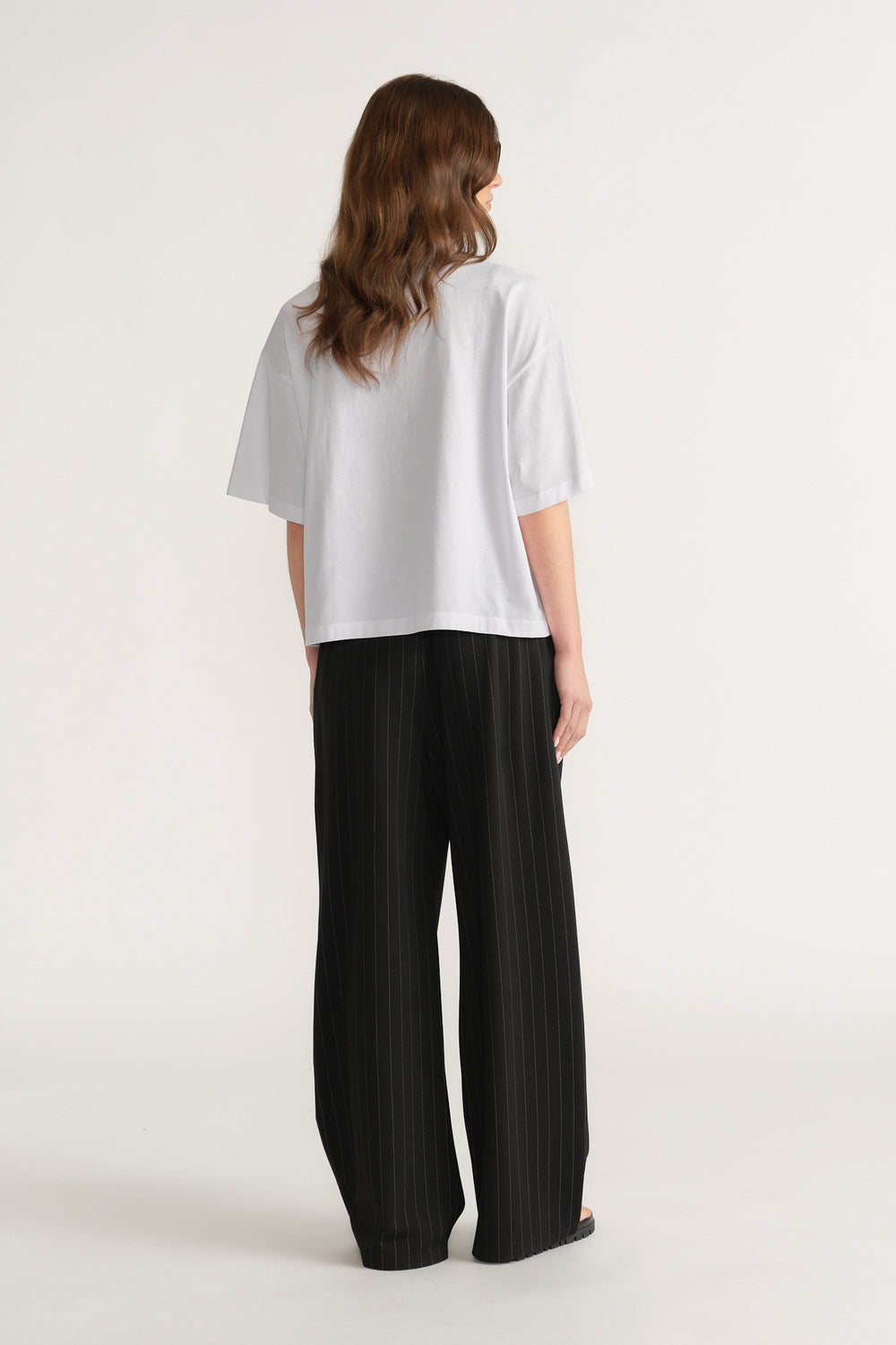 Back view of a woman in an oversized white tee and black wide-leg pleated pants