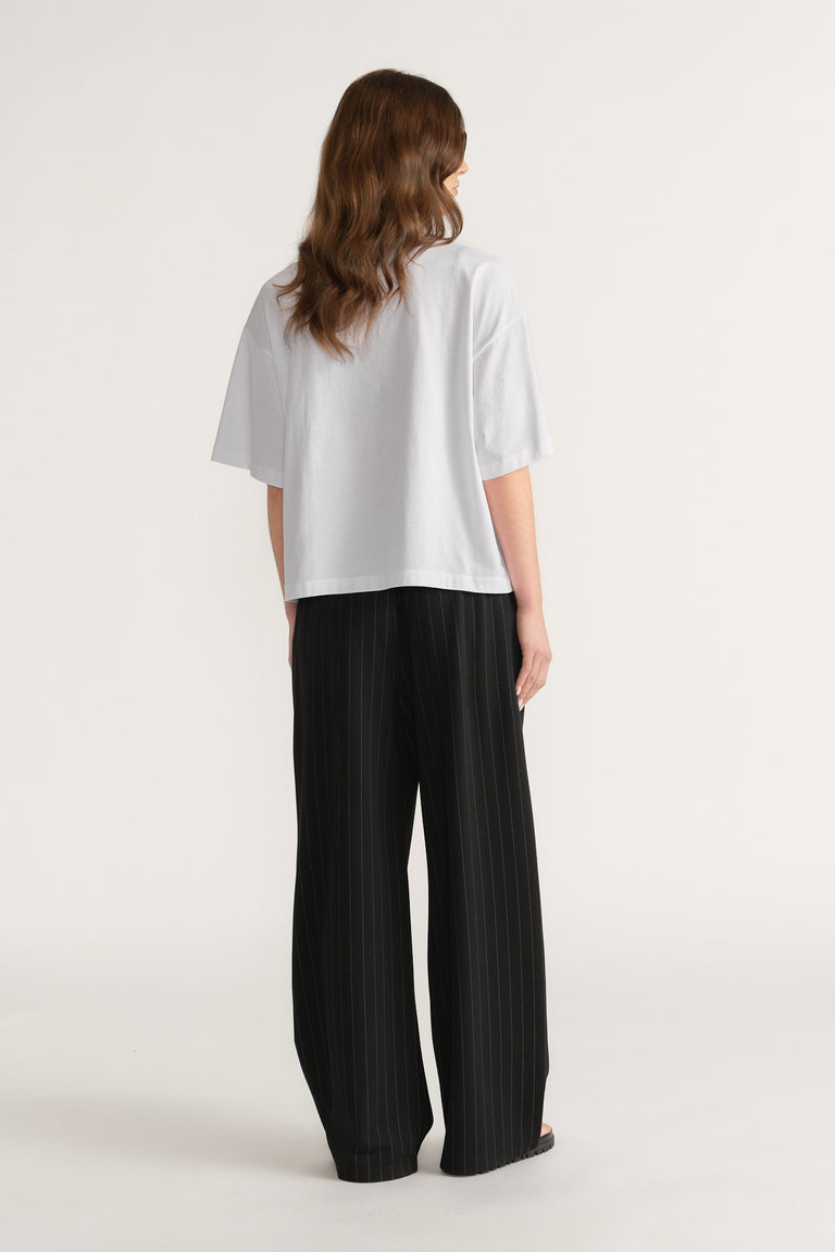 Back view of a woman in an oversized white tee and black wide-leg pleated pants
