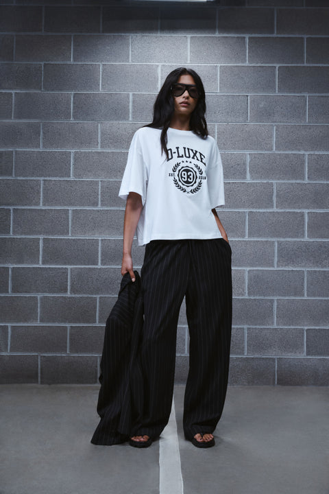 Woman wearing black pinstripe wide leg pants with a white graphic tee and flat sandals