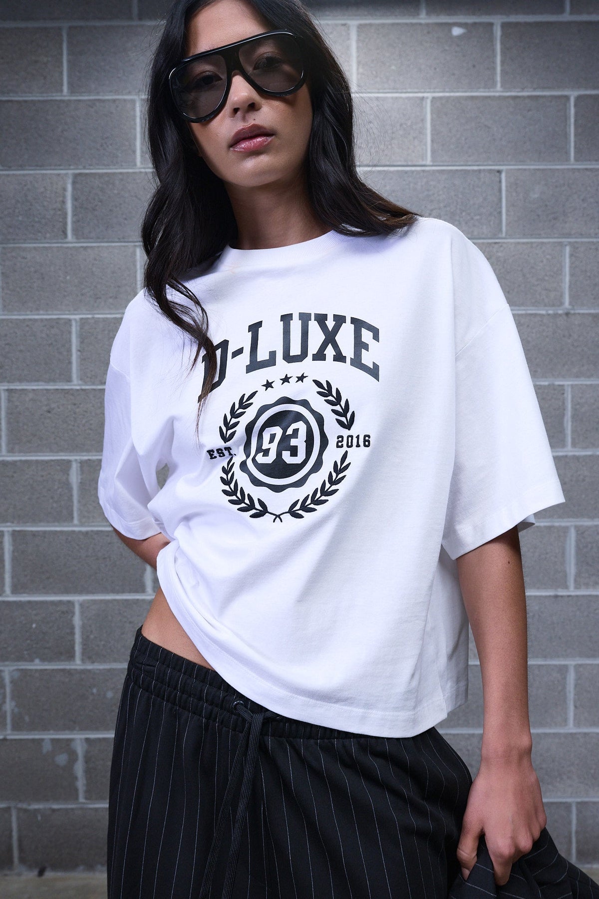 Woman wearing an oversized white graphic tee with black pinstripe pants and sunglasses