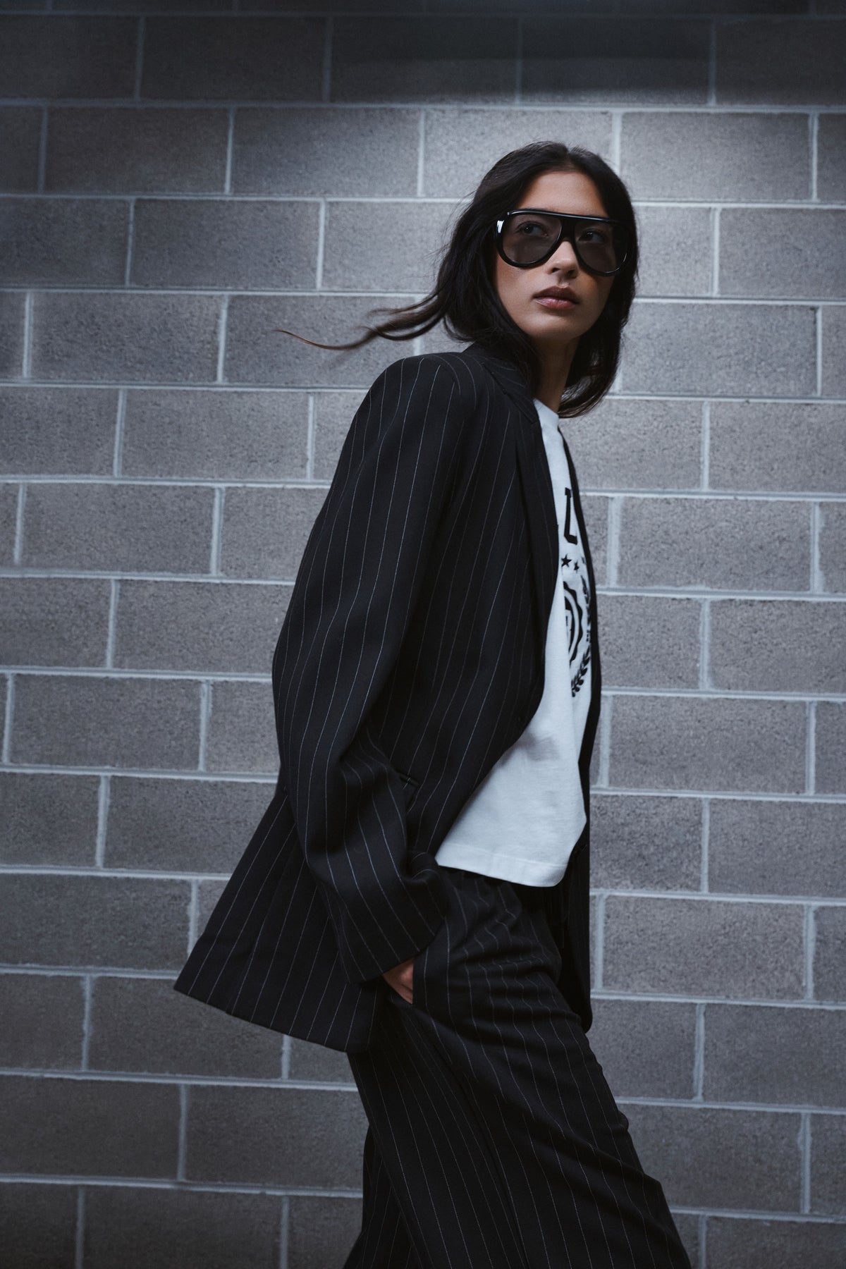 Woman in a black pinstripe blazer and matching trousers over a white graphic tee and sunglasses