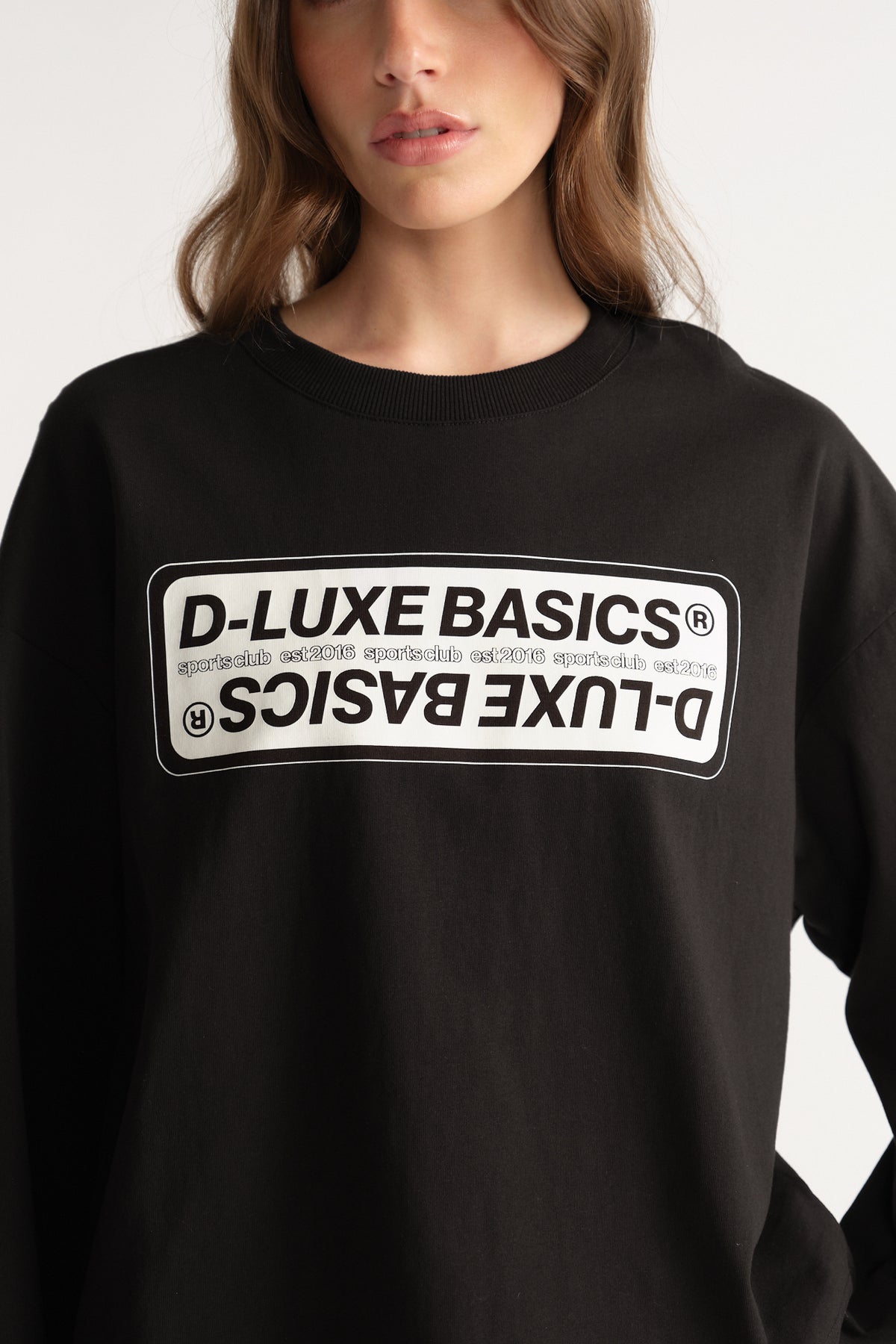 Woman wearing a black oversized long sleeve tee with D-Luxe Basics graphic print