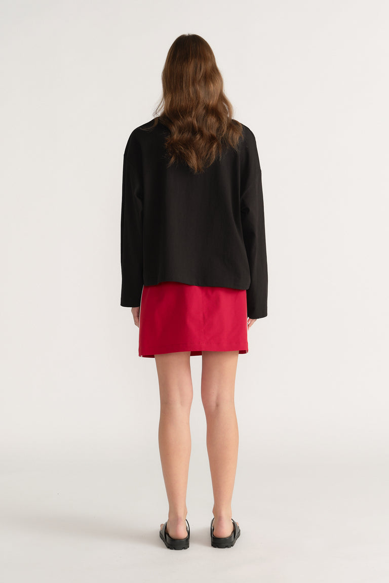 Back view of a model wearing a black oversized long sleeve tee with a red mini skirt