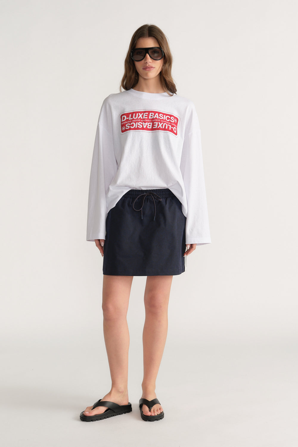 Woman wearing a white oversized long sleeve graphic tee with black shorts and flat sandals