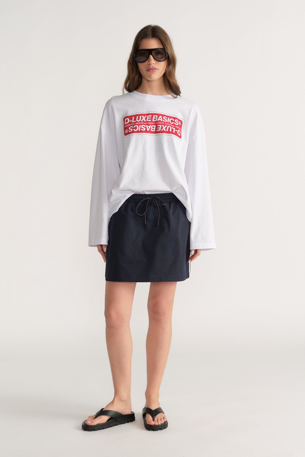 Woman wearing a white oversized long sleeve graphic tee with black shorts and flat sandals
