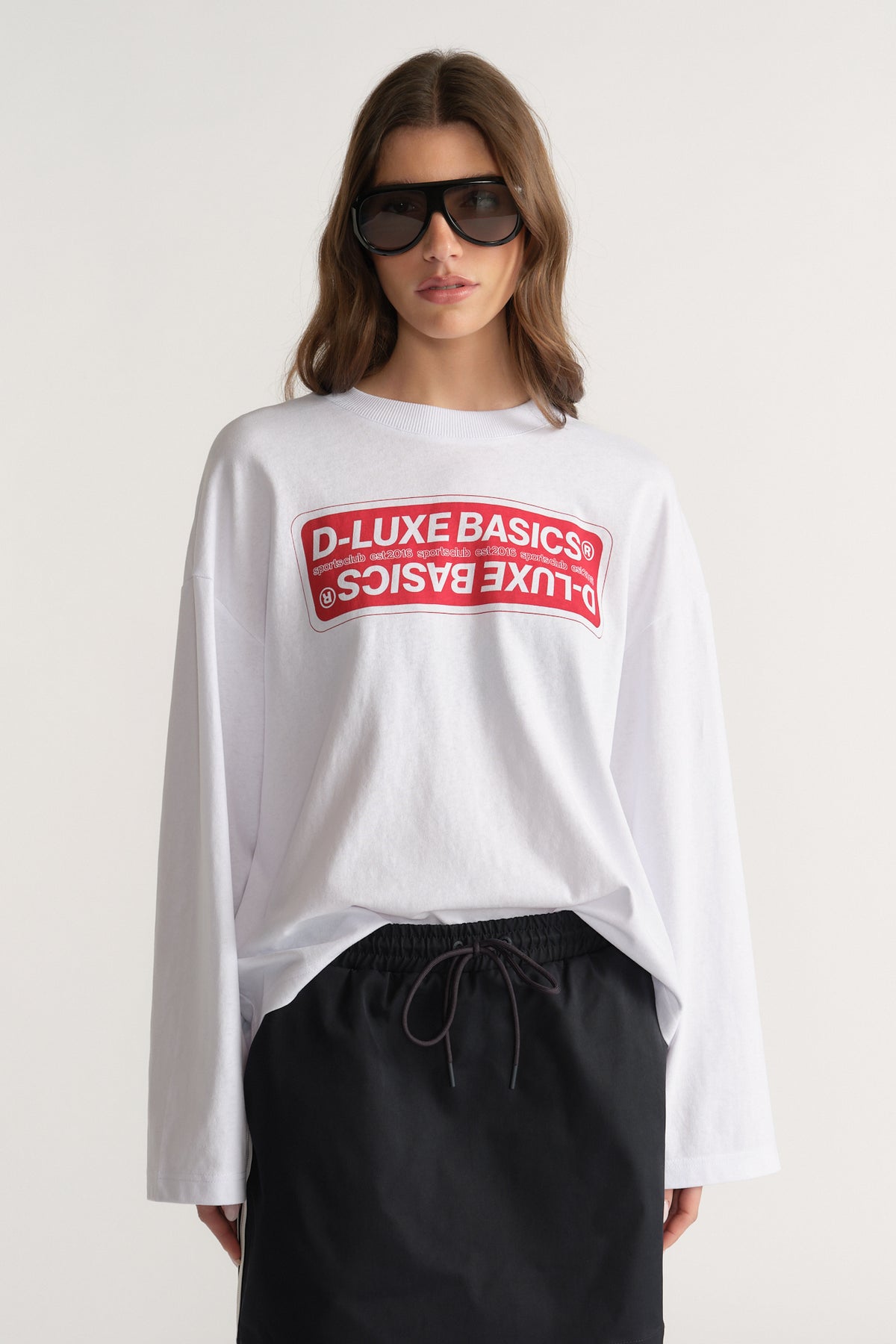 Woman wearing an oversized white D-Luxe graphic long sleeve tee with black drawstring pants and sunglasses
