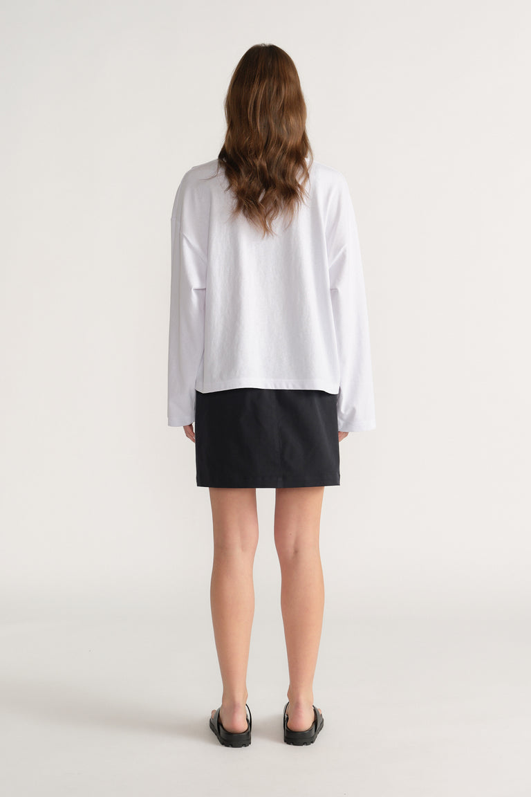 Back view of a woman wearing a relaxed white oversized long sleeve tee with black shorts