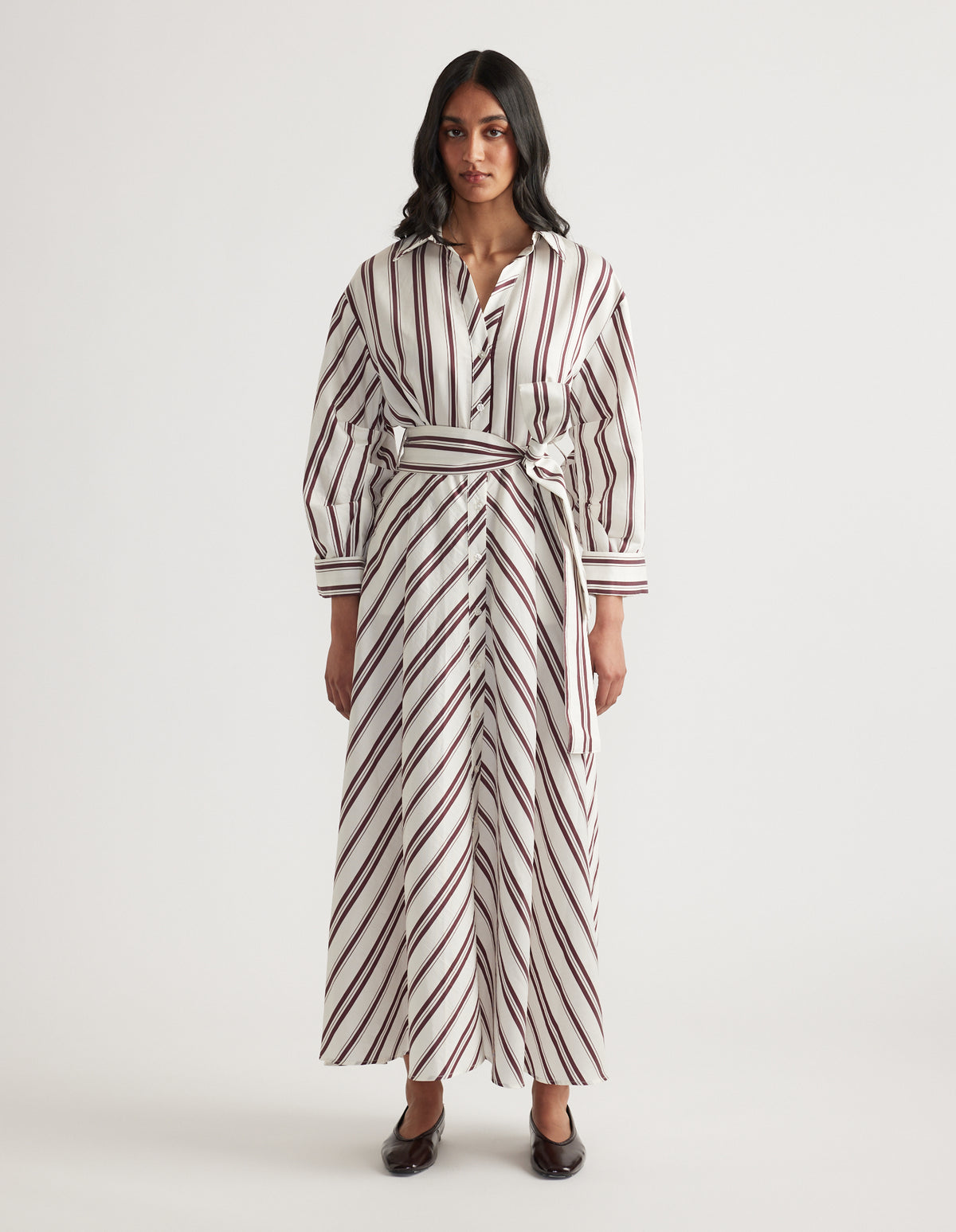 Woman wearing a striped long sleeve shirt dress with a collared neckline, waist tie, midi hem and black flats