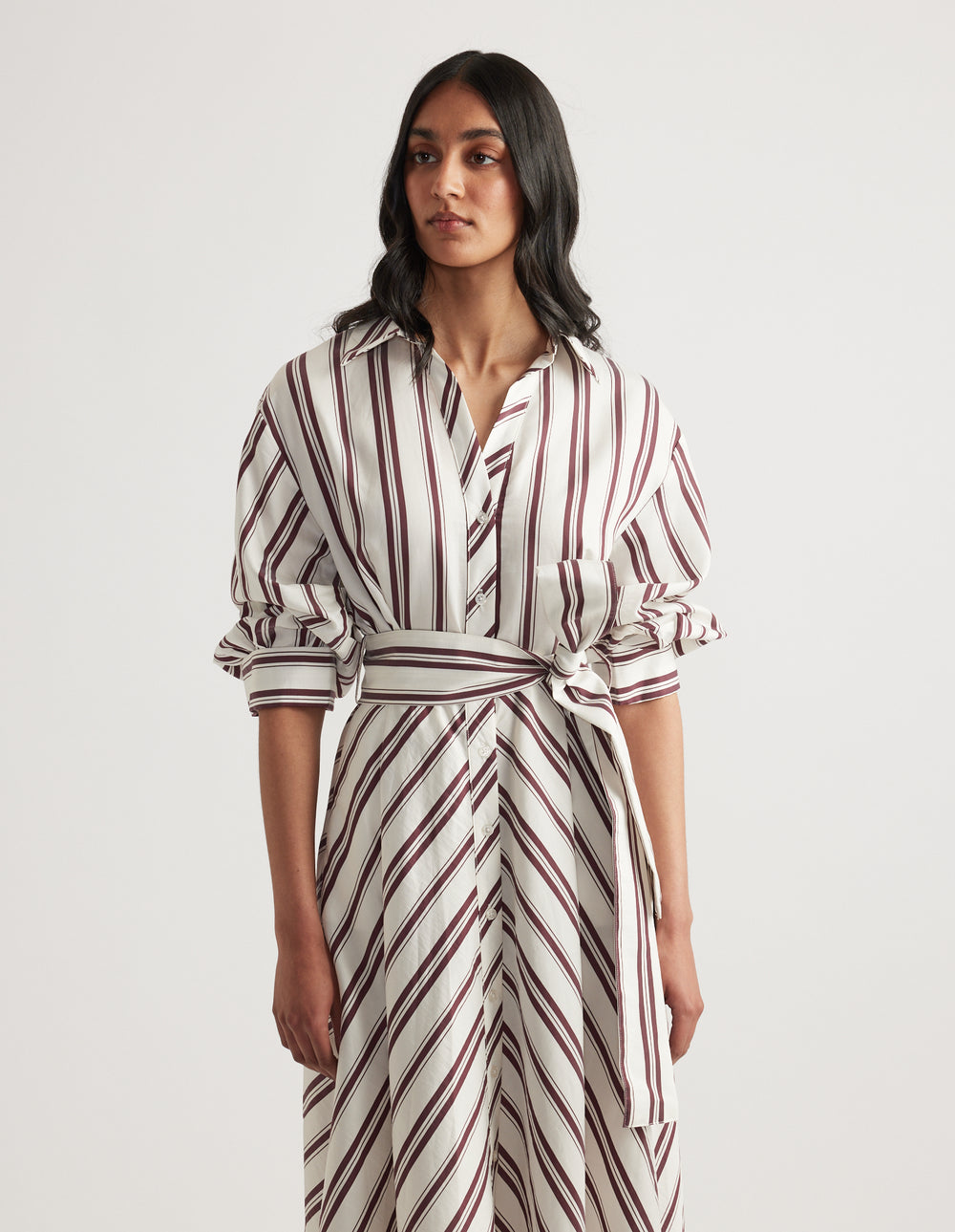 Woman wearing a striped midi shirt dress with long sleeves, collar, button front and adjustable waist tie