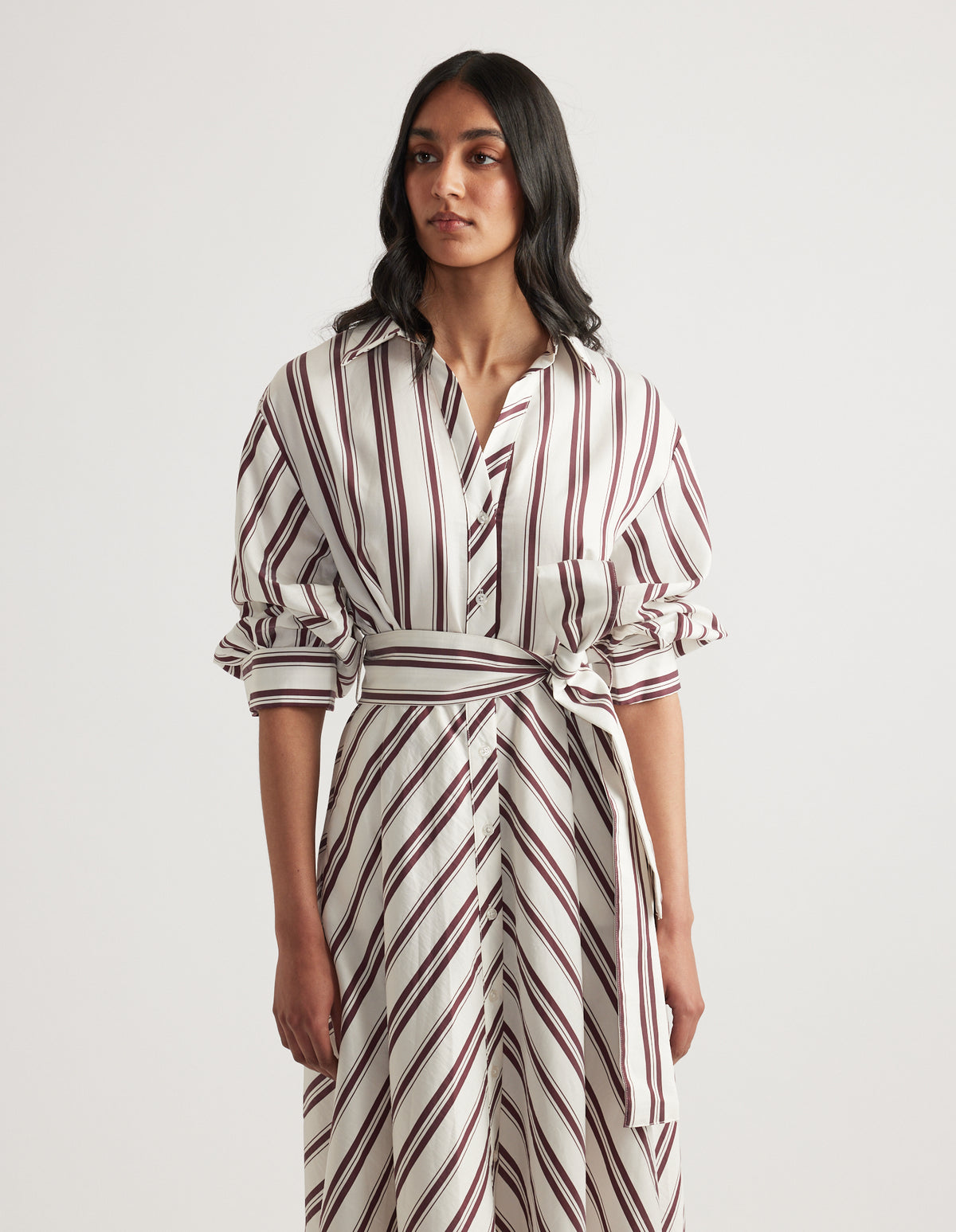 Woman wearing a striped midi shirt dress with long sleeves, collar, button front and adjustable waist tie