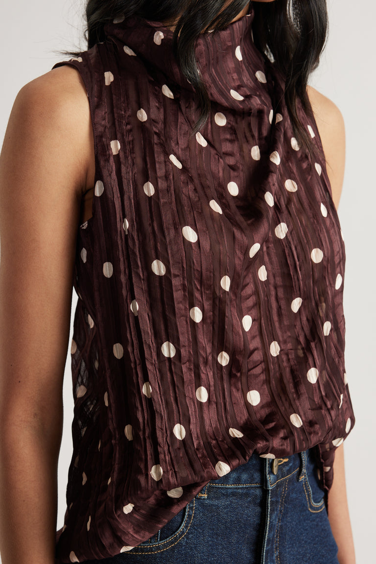 Woman wearing a burgundy textured sleeveless top with cream spots and dark blue jeans