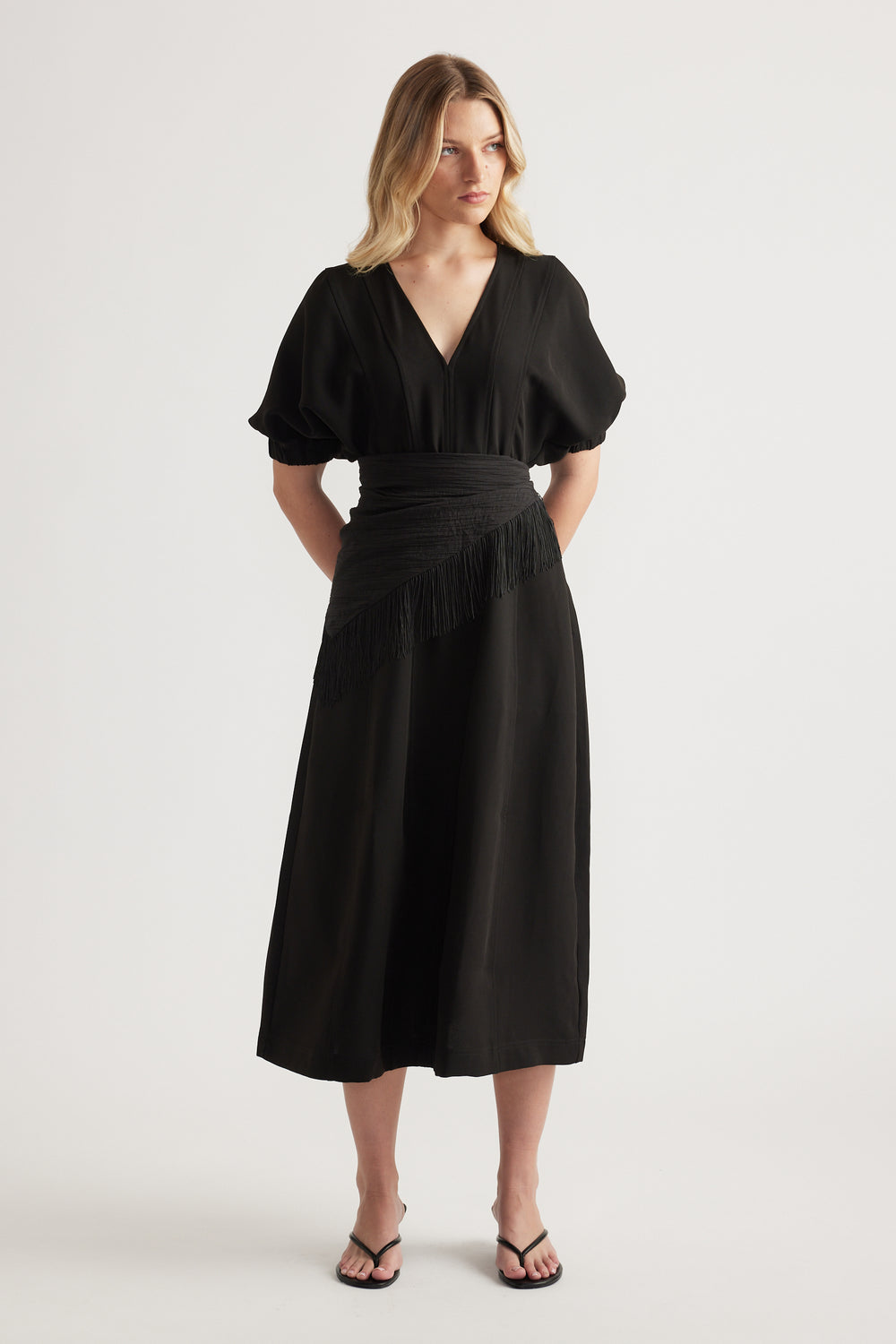 Woman wearing a black V neck midi dress with puff sleeves, panelled waist and an A line skirt