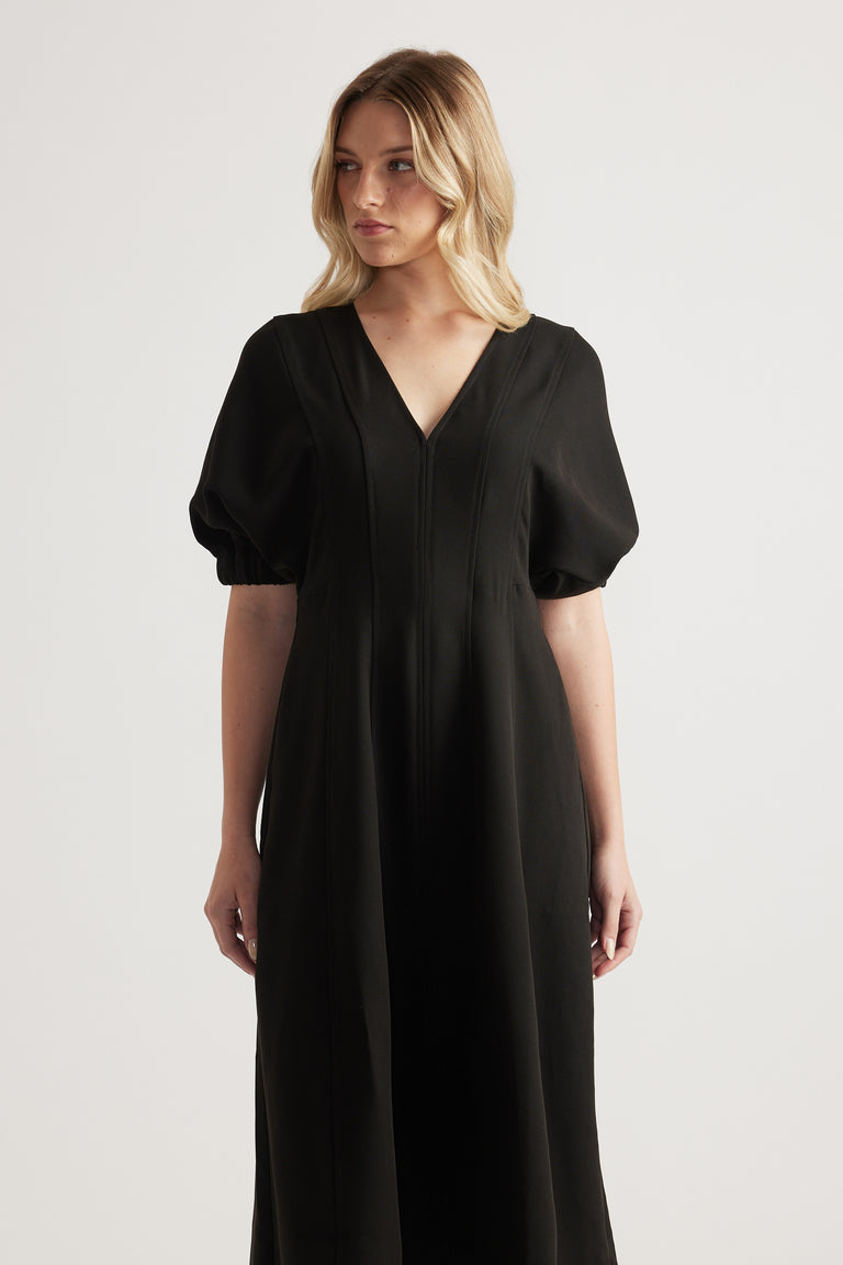 Woman wearing a black V-neck midi dress with short puff sleeves and an A-line silhouette