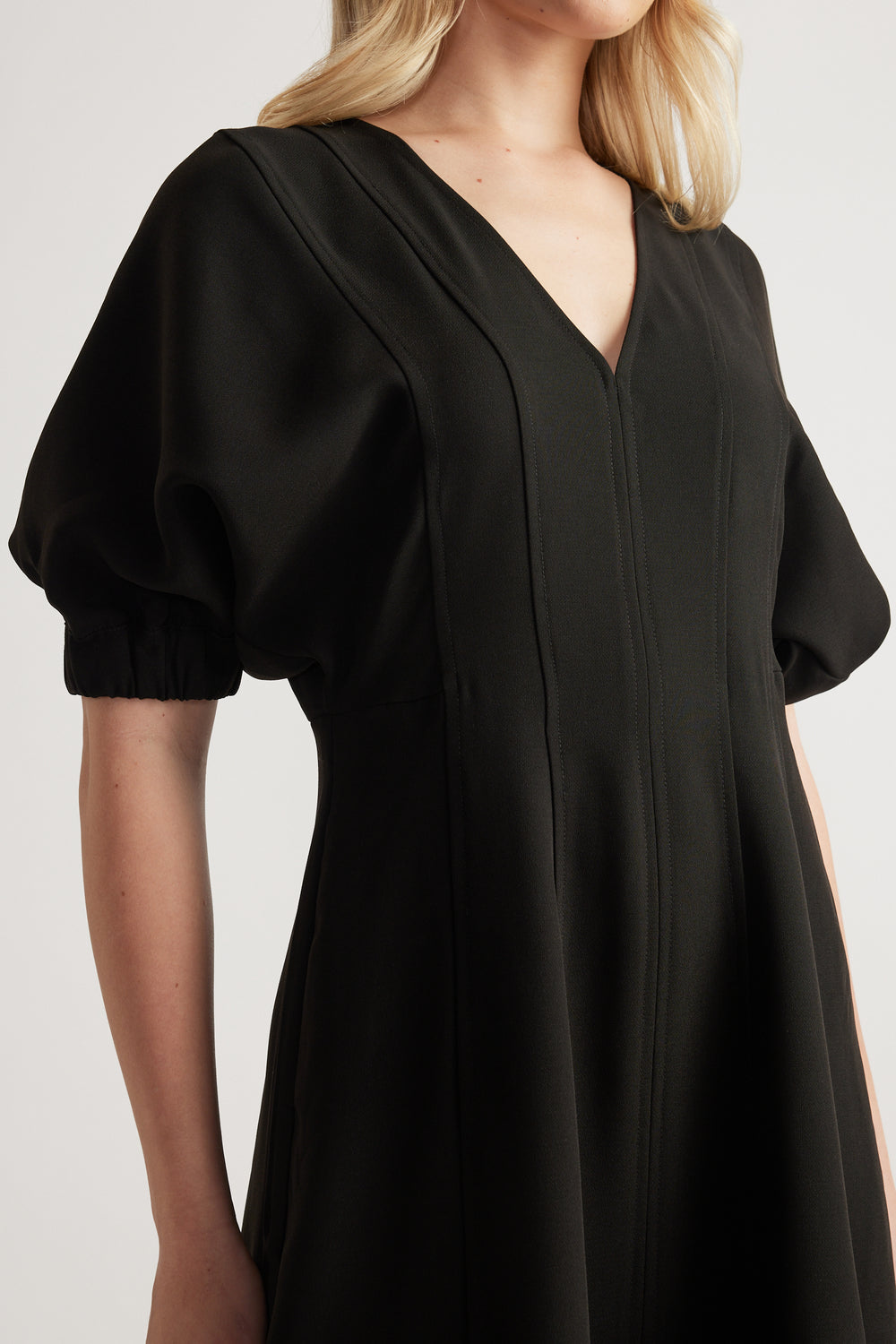 Woman wearing a black panelled midi dress with puff sleeves and a V neckline