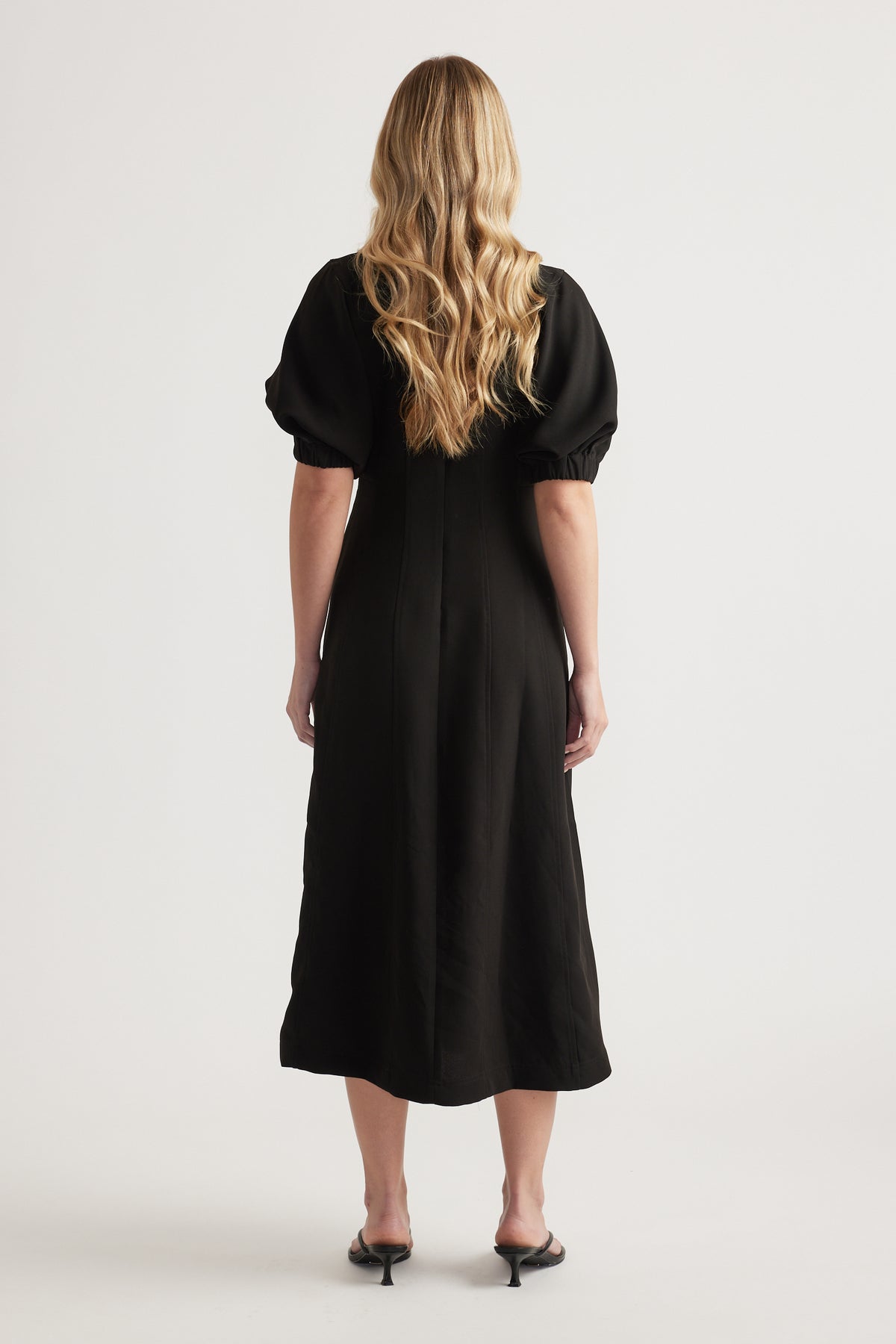 Back view of a woman wearing a black midi dress with puff sleeves and an A-line silhouette
