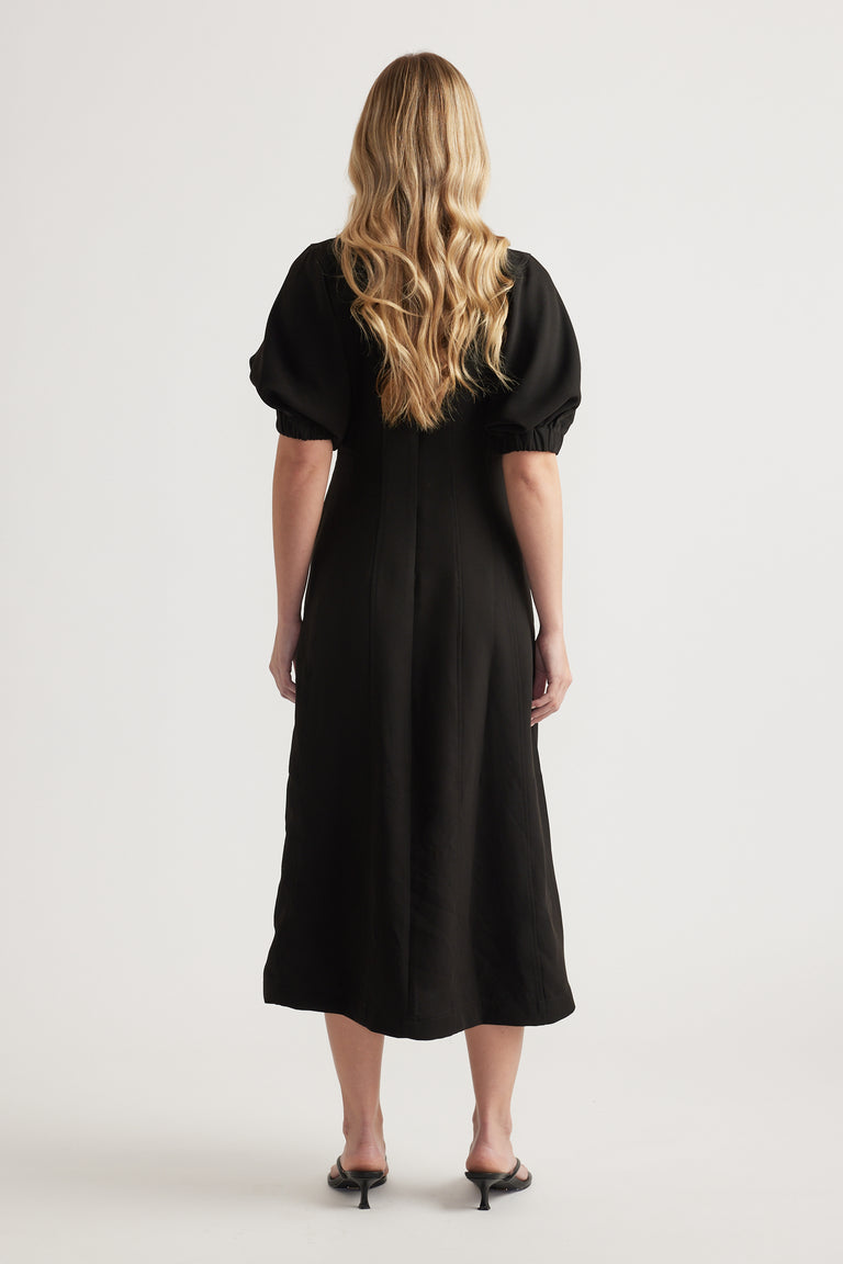 Back view of a woman wearing a black midi dress with puff sleeves and an A-line silhouette