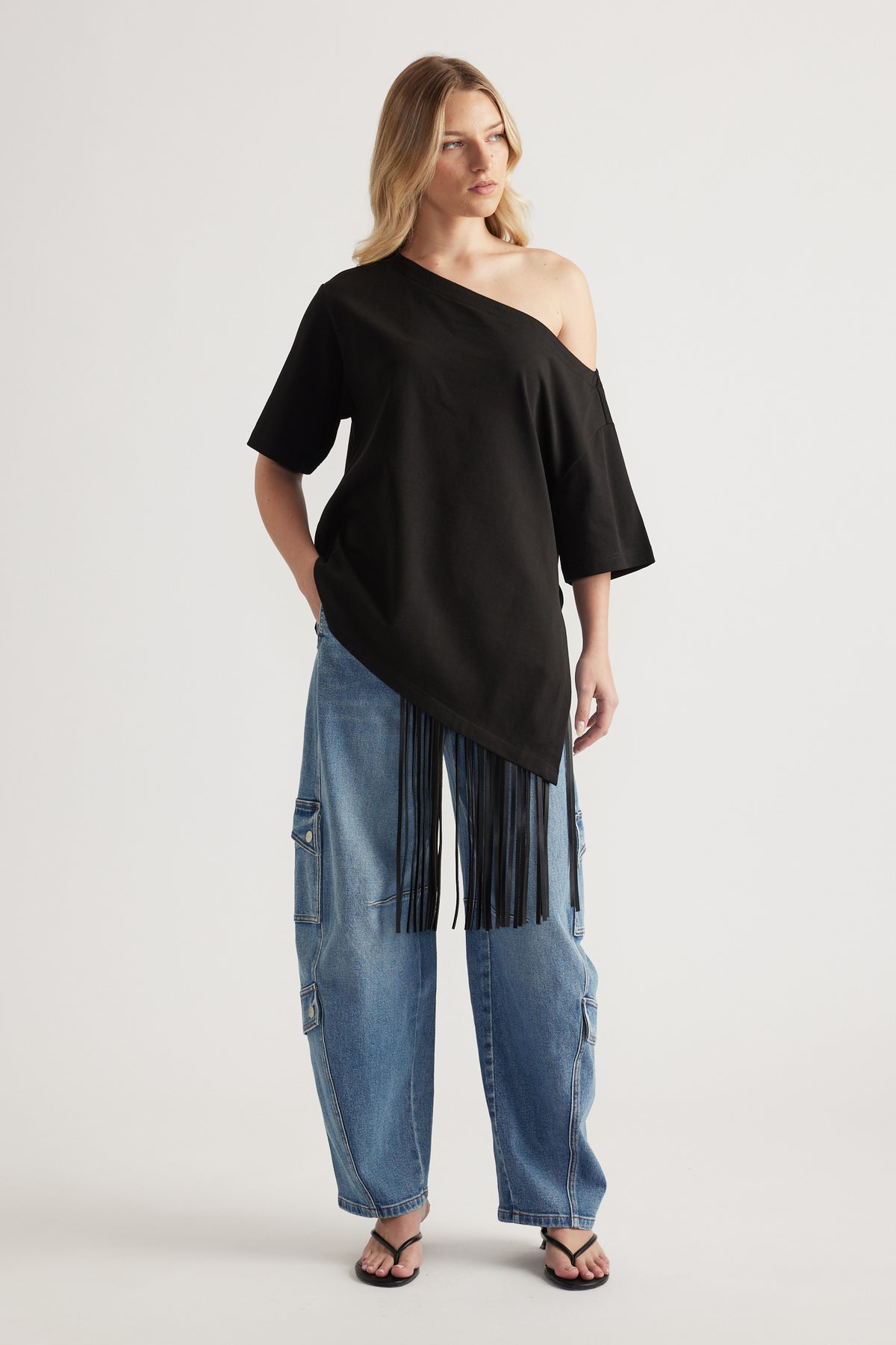 Woman wearing blue high rise barrel leg cargo jeans with a black off shoulder top and flat sandals
