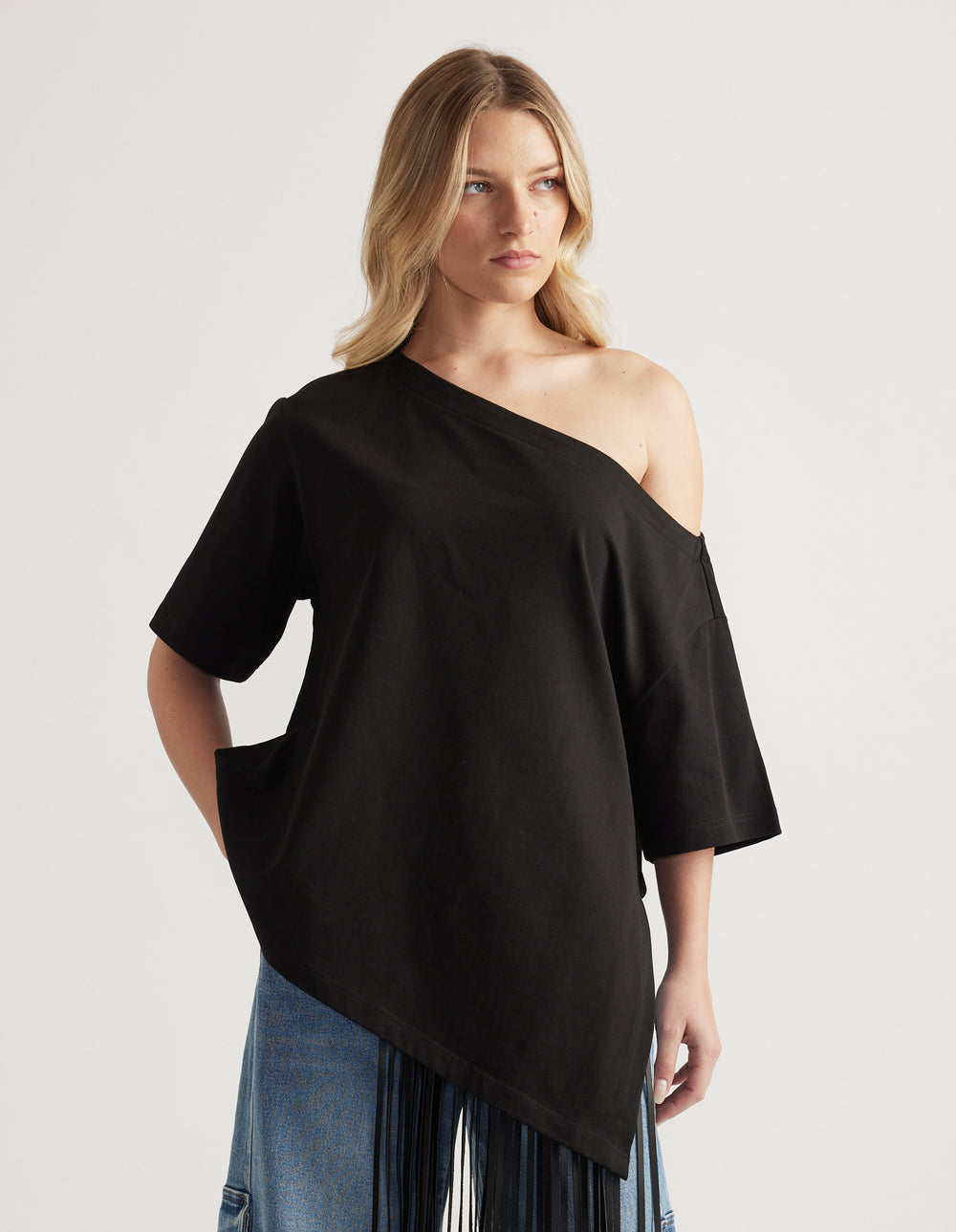 Woman wearing a relaxed black tee with an asymmetric neckline and hem, styled with blue jeans