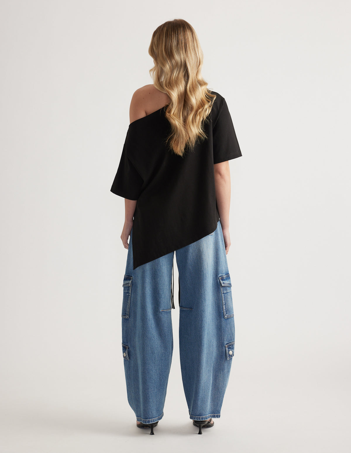 Woman wearing a black relaxed fit asymmetric tee with one shoulder exposed and wide leg cargo jeans