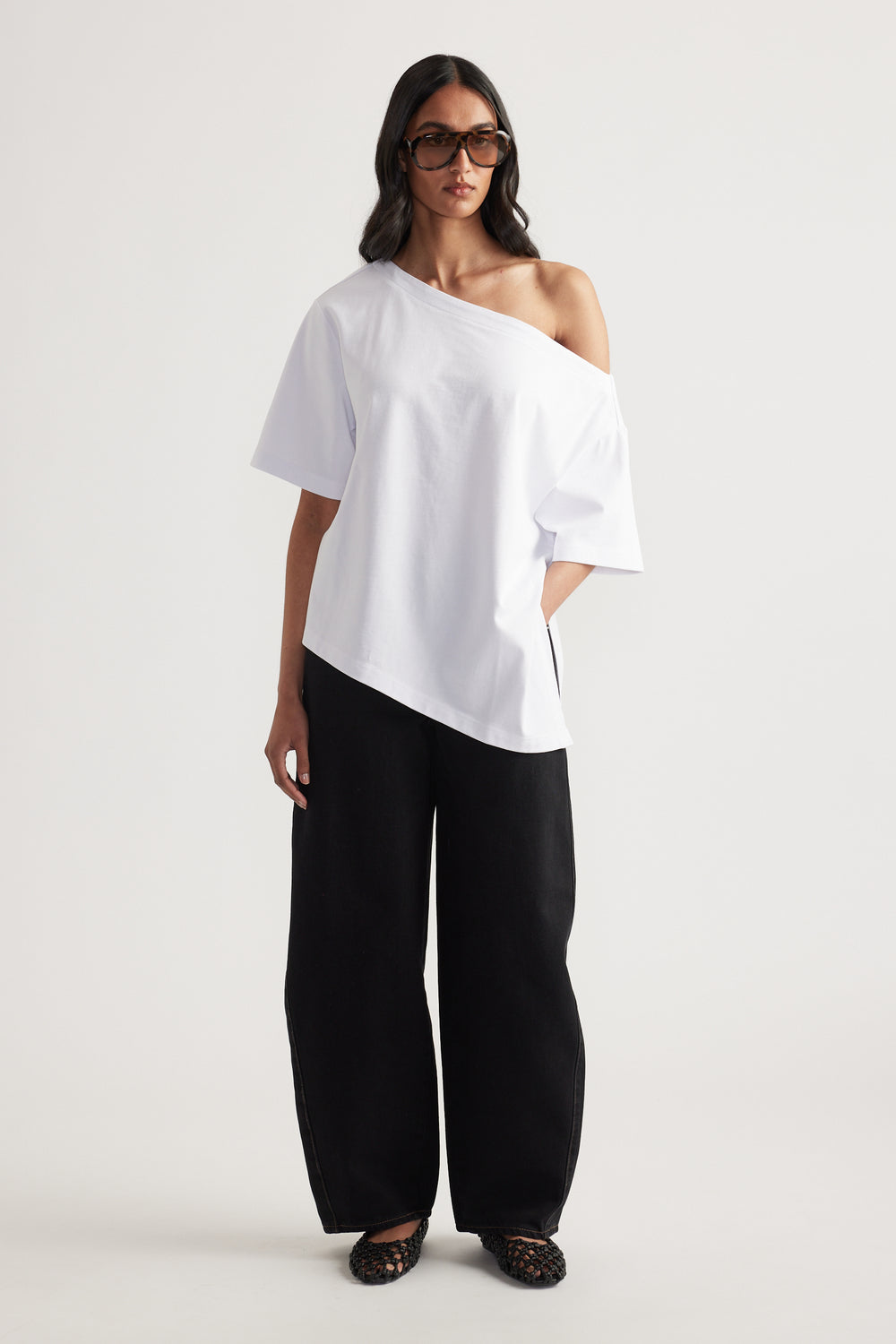Woman wearing a white relaxed fit tee with asymmetric neckline and hem, black wide leg pants and sunglasses