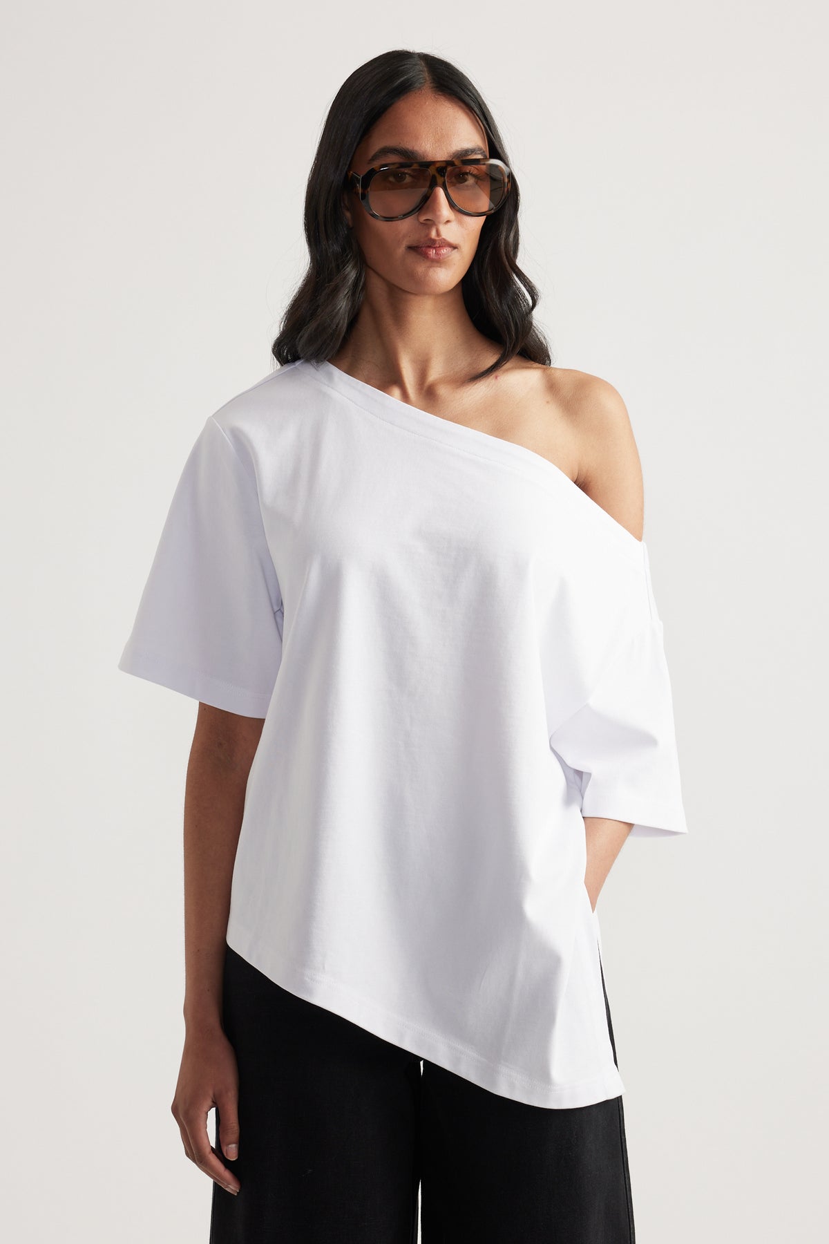 Woman wearing a white relaxed fit tee with asymmetric neckline and hem, black pants and sunglasses