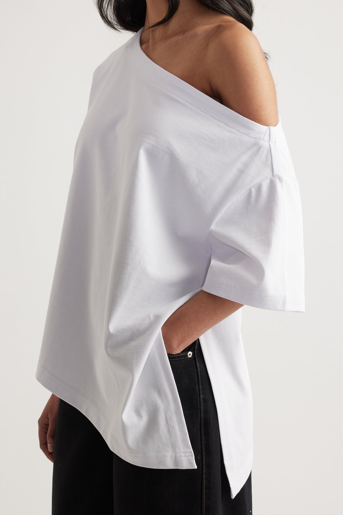 Woman wearing a white relaxed fit tee with asymmetric neckline and hem styled with black jeans