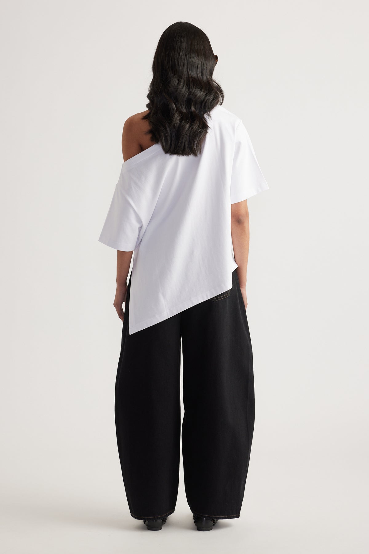Woman seen from behind wearing a white asymmetric neckline tee with uneven hem and black wide leg pants