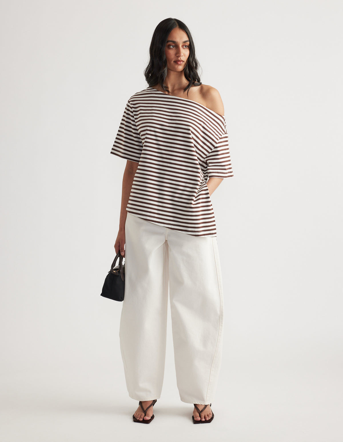 Woman wearing a striped asymmetric neck tee with white wide leg pants black handbag and flat sandals