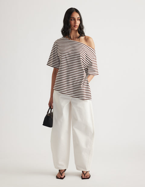 Woman wearing a striped asymmetric neck tee with white wide leg pants black handbag and flat sandals