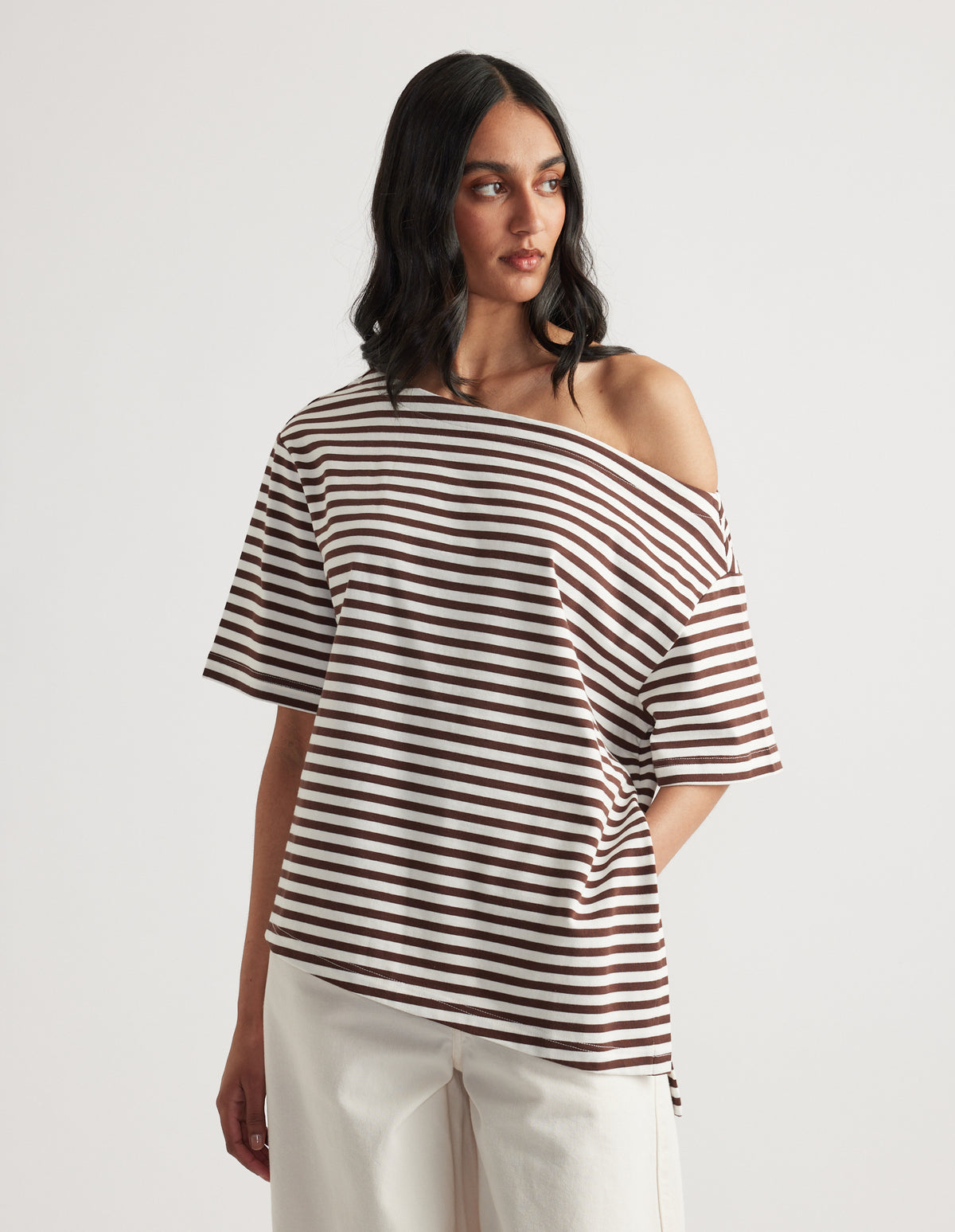 Woman wearing a relaxed brown and white striped tee with an asymmetric neckline and white pants