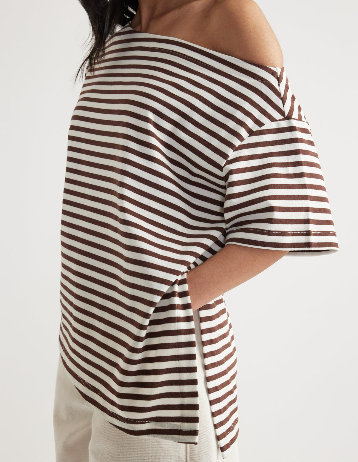 Woman wearing a brown and white striped relaxed fit tee with asymmetric neckline and hem, styled with white pants