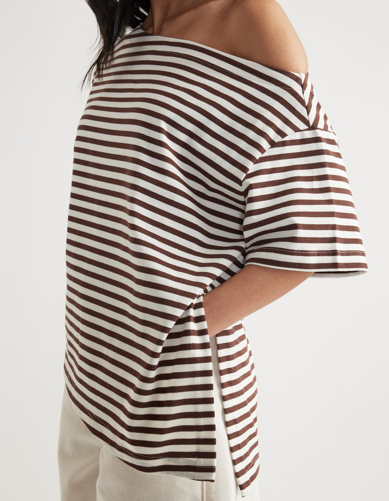 Woman wearing a brown and white striped relaxed fit tee with asymmetric neckline and hem, styled with white pants