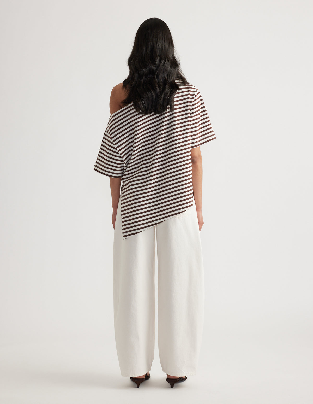 Back view of woman wearing a brown and white striped relaxed fit tee with an asymmetric hem and wide leg white pants