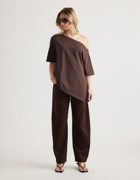 Woman wearing a brown relaxed fit tee with an asymmetric neckline and hem, styled with matching pants and sunglasses