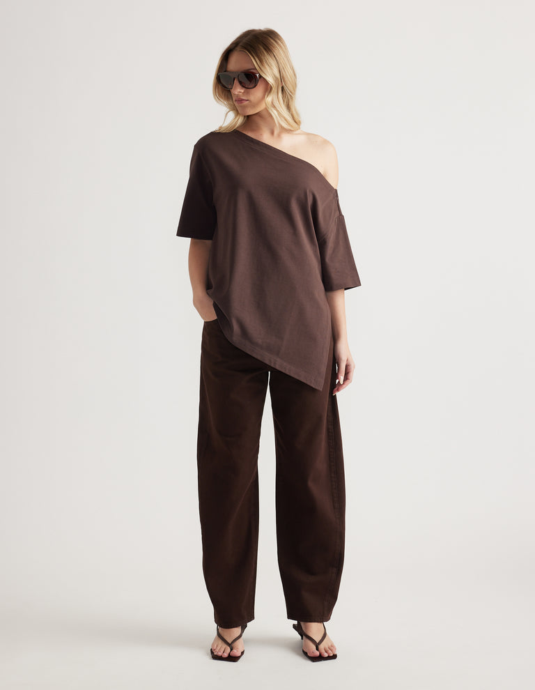 Woman wearing a brown relaxed fit tee with an asymmetric neckline and hem, styled with matching pants and sunglasses