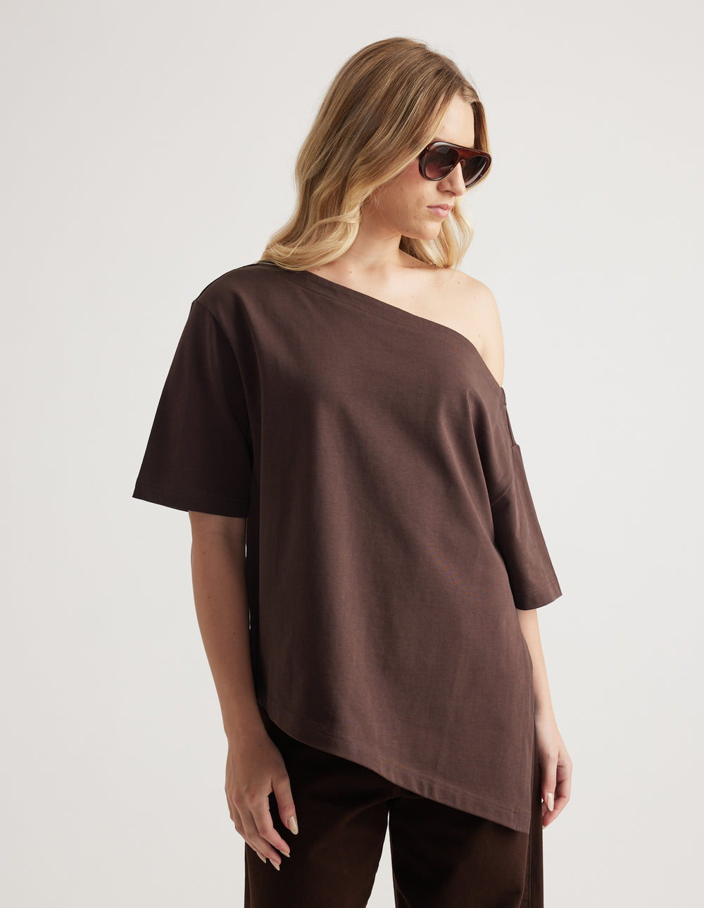 Woman wearing a relaxed brown tee with an asymmetric neckline and hem, styled with matching pants and sunglasses