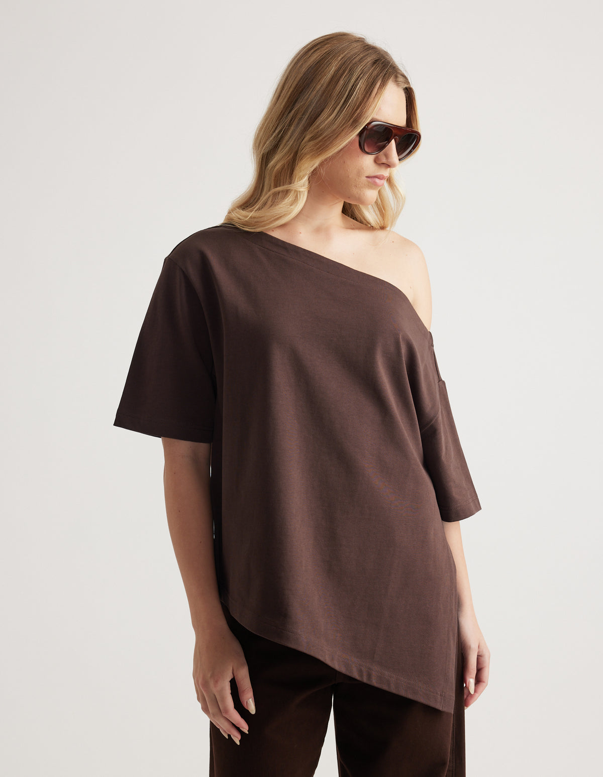 Woman wearing a relaxed brown tee with an asymmetric neckline and hem, styled with matching pants and sunglasses