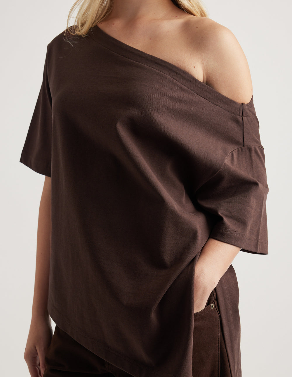 Woman wearing a relaxed dark brown tee with an asymmetric neckline and hem, styled with matching pants