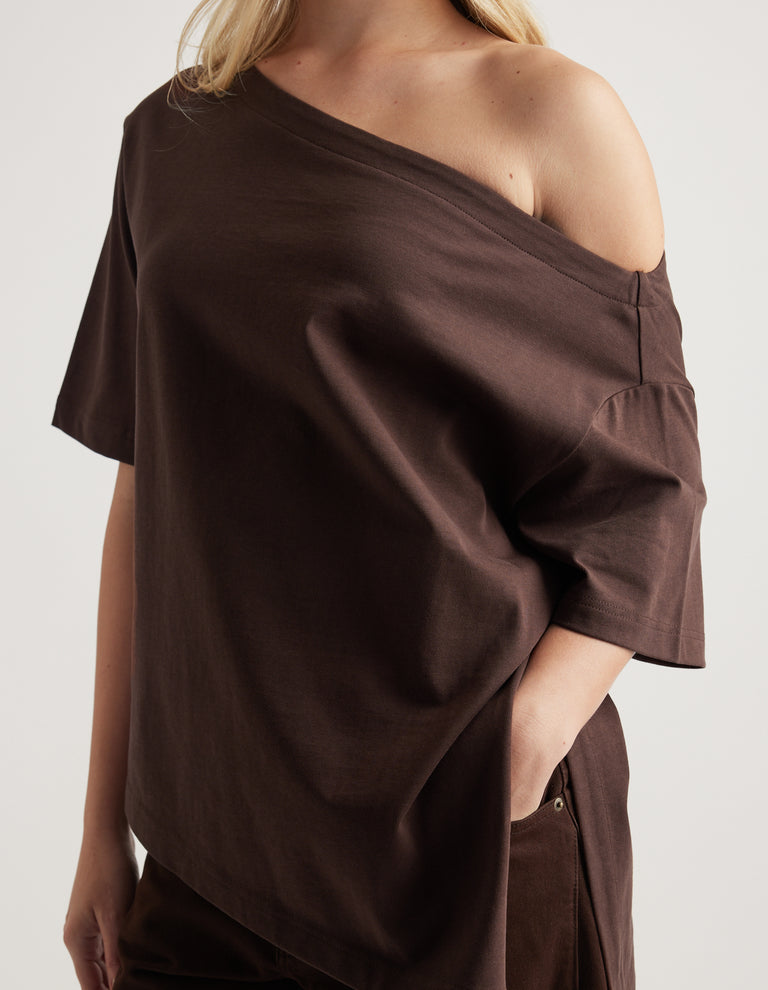 Woman wearing a relaxed dark brown tee with an asymmetric neckline and hem, styled with matching pants