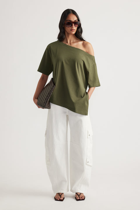 Woman styling an olive asymmetric off shoulder tee with white cargo pants, sunglasses, woven shoulder bag and sandals