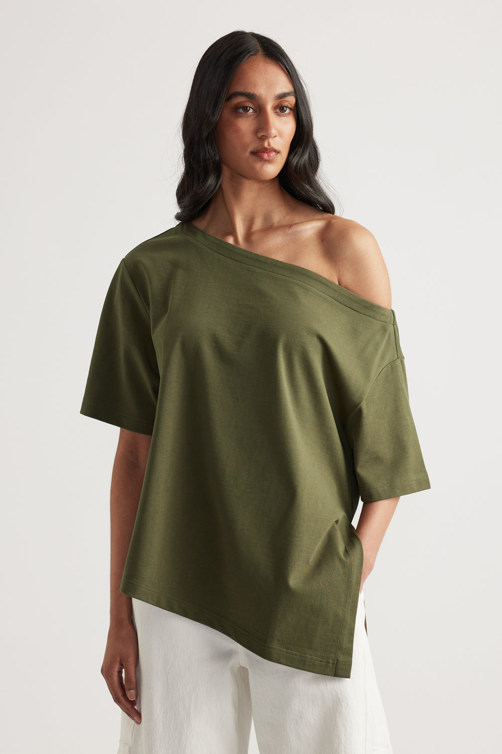 Woman wearing an olive green asymmetric neckline tee with an uneven hem and white pants