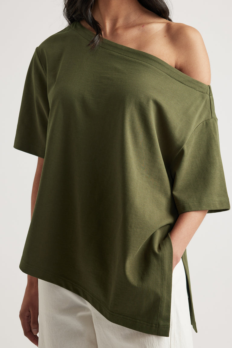 Woman wearing an olive green relaxed fit tee with an asymmetric neckline and hem, styled with white pants